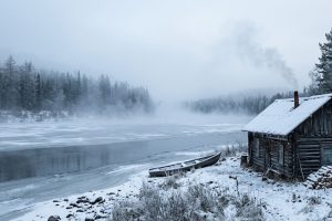 Берег сибирской реки с деревянной избой в морозное утро